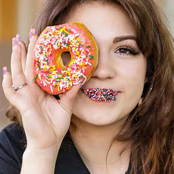 Senior girl holding a sprinkle donut over her eye with colorful sprinkles on her lips.