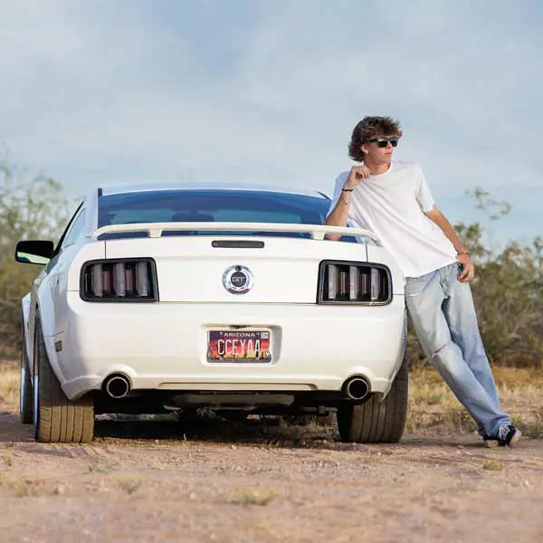 Senior guy leaning against his white Mustang during outdoor desert senior session.