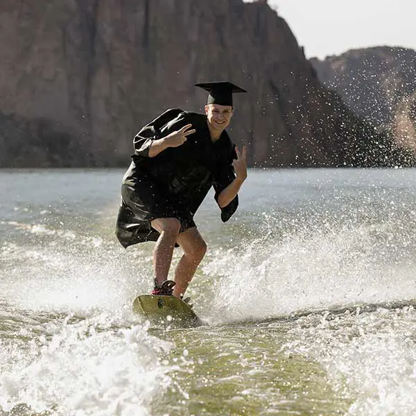 High school senior guy wakeboarding in graduation cap and gown at Canyon Lake.