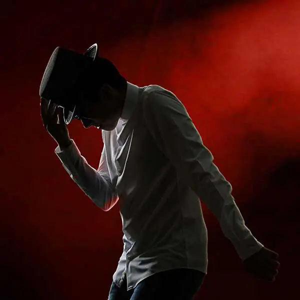 Silhouette of senior guy on stage tipping his hat under dramatic red lighting.