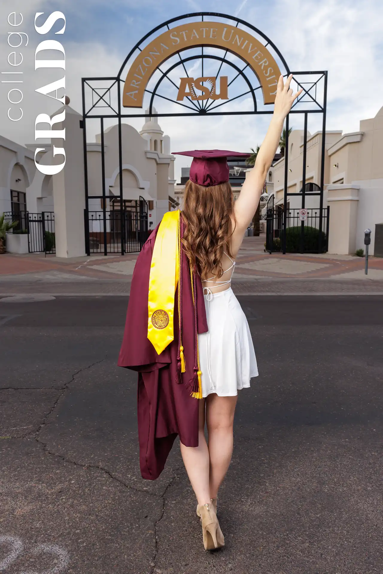 College graduate in cap and gown holding up a peace sign at the ASU arch in Downtown Phoenix, Arizona