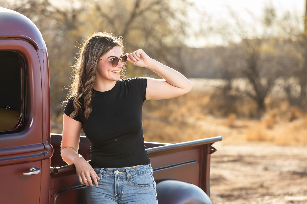Before edit: Senior portrait of a girl standing next to a vintage truck in Mesa, Arizona, with sunlight highlighting her outfit and sunglasses.