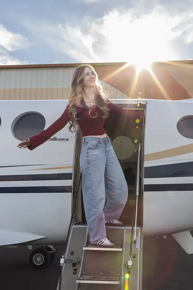 Teen girl stepping off a private jet with the sun flaring behind her, captured during a senior photoshoot.
