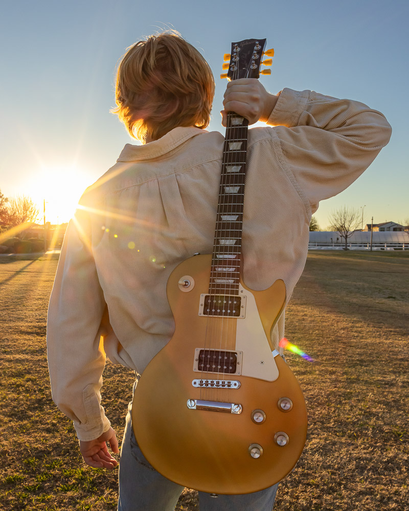 Senior boy holds a gold electric guitar over his shoulder during a sunset photo shoot in East Mesa.