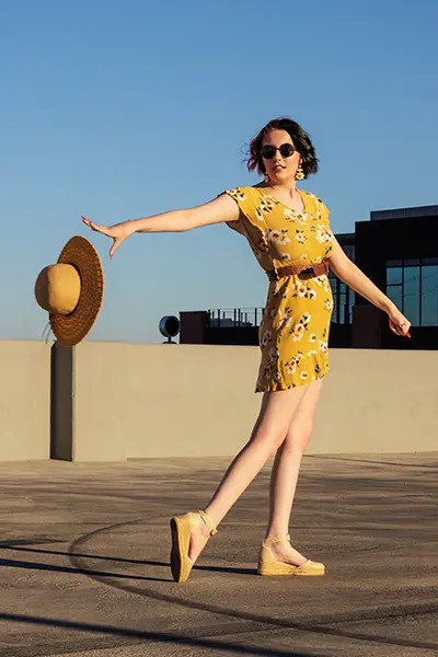 Teen girl in a yellow floral dress playfully tossing her hat during an editorial-style senior photo shoot in Arizona.