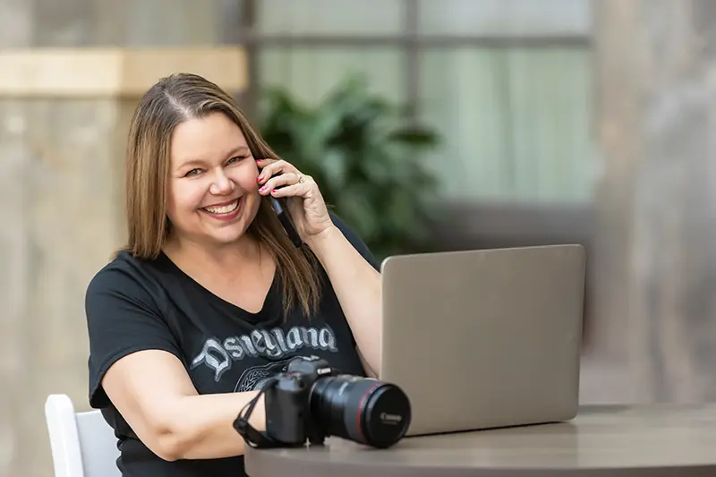 Michelle Robertson senior photographer in Mesa Arizona smiling during a phone consultation with camera and laptop.