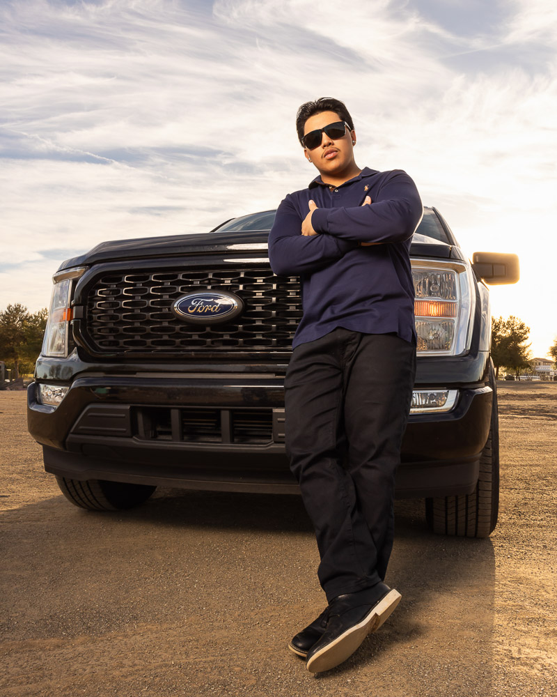 Senior boy leaning against a black Ford truck at sunset for senior portraits in Mesa, Arizona.