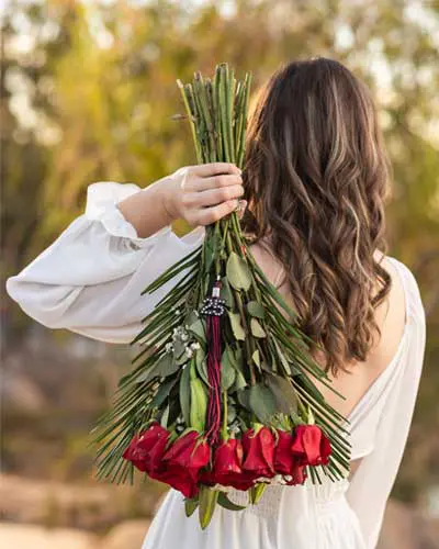 High school senior girl holding a bouquet of roses with her graduation tassel in an outdoor photo session.
