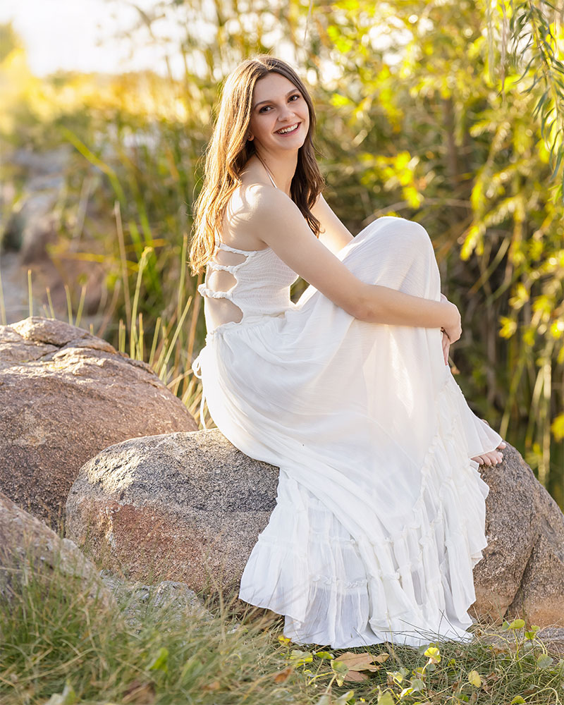 Senior girl sitting on a rock in a white flowy dress for outdoor senior portraits in San Tan Valley, Arizona.