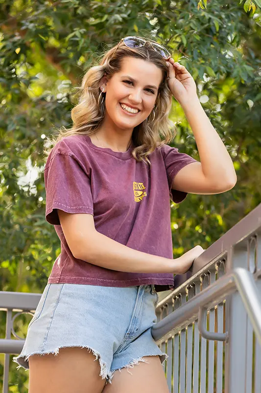 Smiling teen girl in a maroon shirt and jean shorts during her senior photo session in Chandler, Arizona.