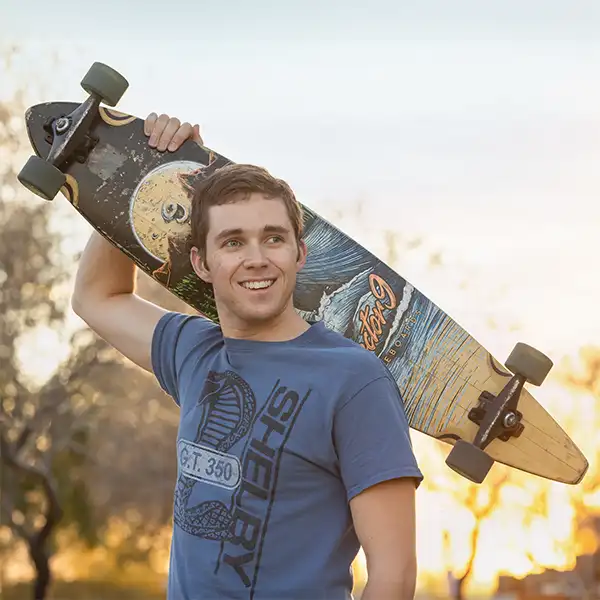 College senior guy holding a longboard over his shoulder at sunset in Arizona.