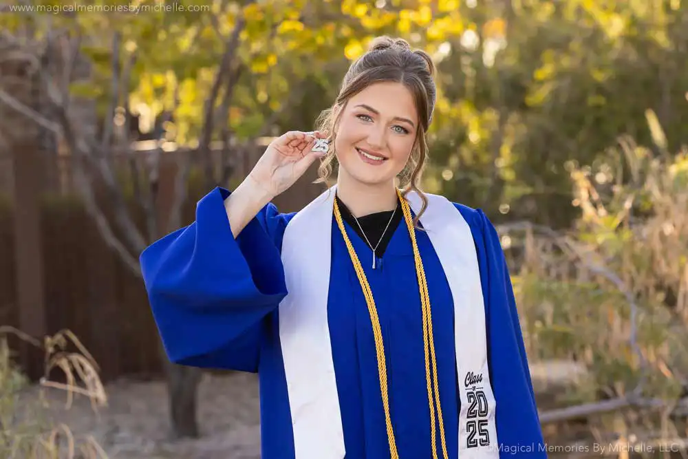 Senior girl in a bright blue cap and gown smiling while holding a Class of 2025 tassel during her senior photo session in Arizona.