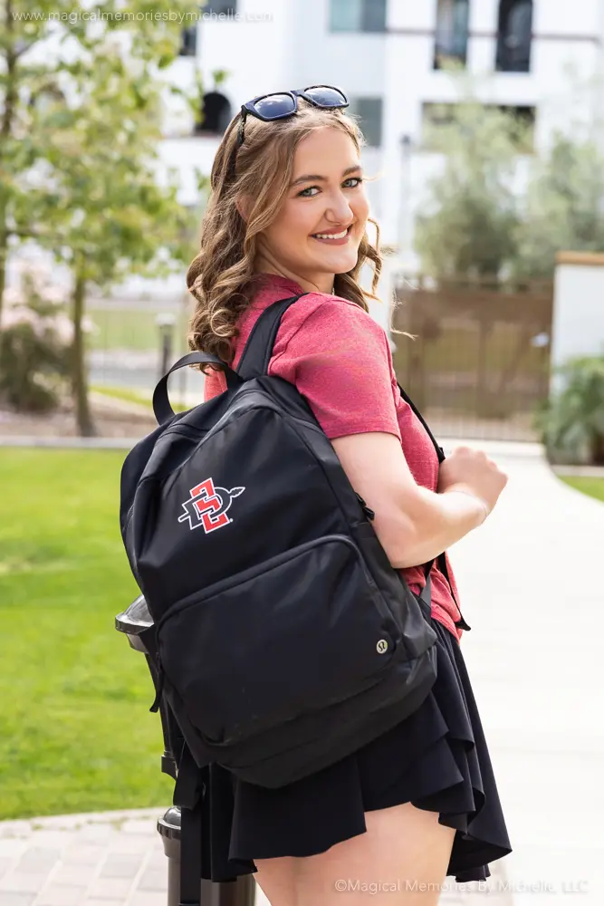 Smiling senior girl with a college backpack walking across campus.