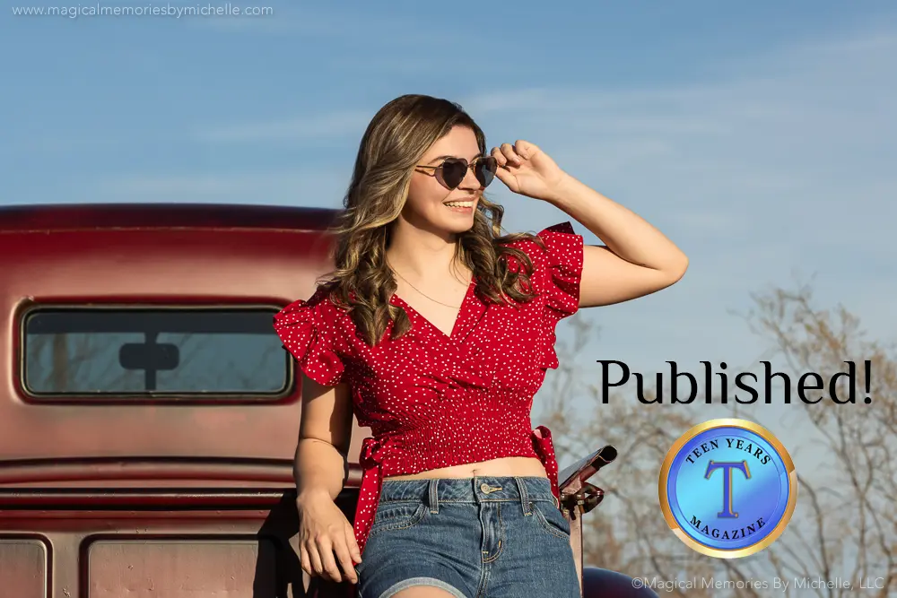 Confident teen girl wearing a red blouse and denim shorts, smiling in front of a vintage red truck during a photo shoot in Mesa, Arizona.