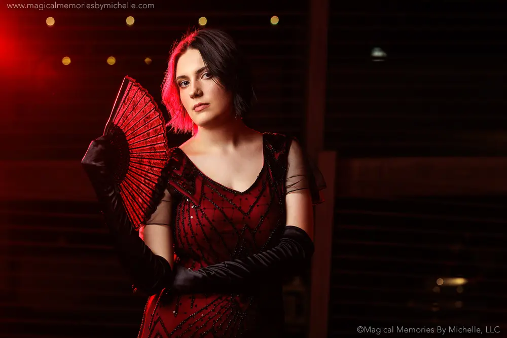 Senior girl in a dramatic red and black beaded dress with gloves and a matching fan for a striking editorial-style photo.