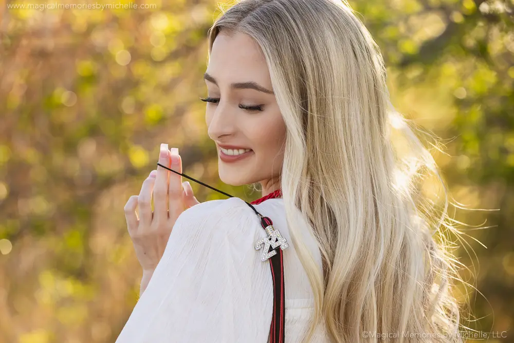 Blonde senior girl smiling while holding her tassel charm over her shoulder during graduation photos in Mesa, Arizona.