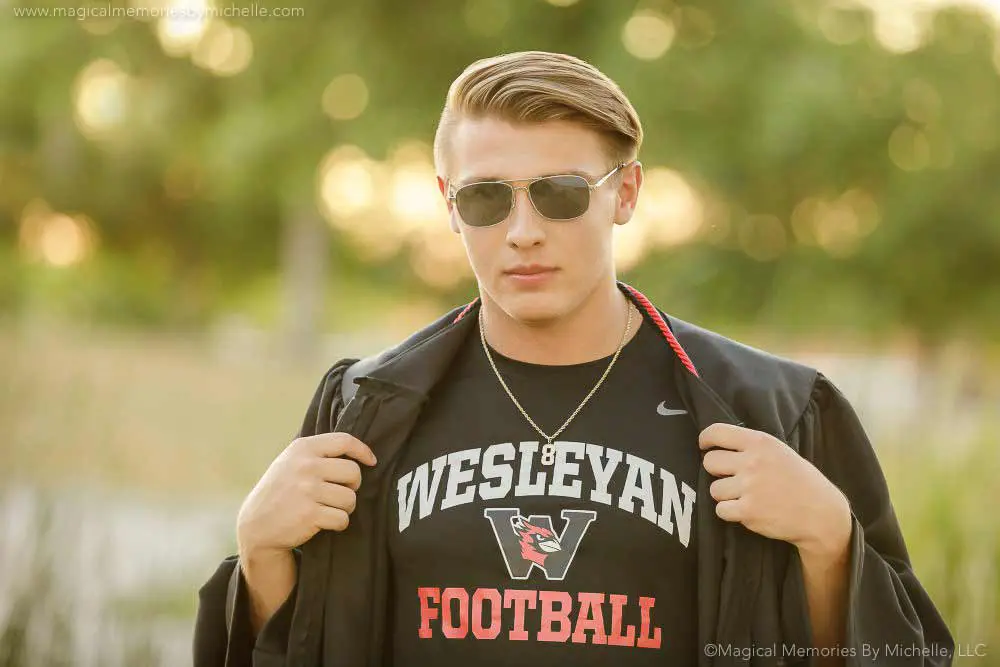 Senior boy wearing sunglasses and a Wesleyan football shirt under his gown during graduation photos in Mesa, AZ.