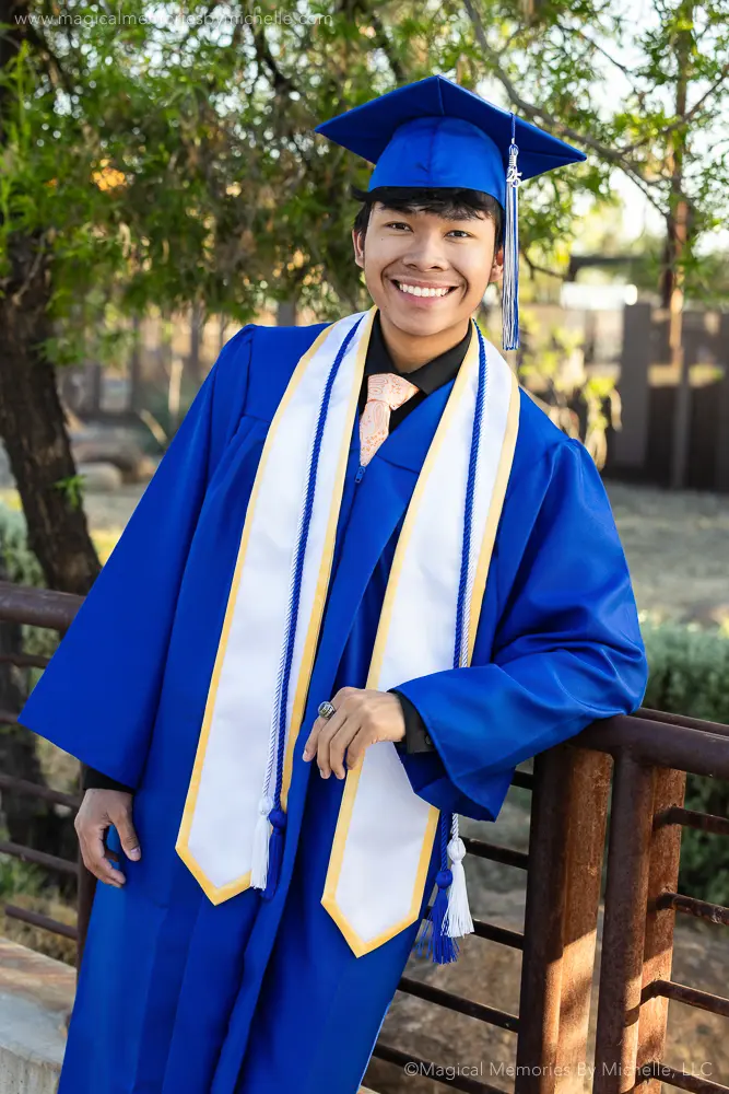Senior guy wearing blue cap and gown with white and gold stole and blue cords for his graduation photo in Mesa, Arizona.