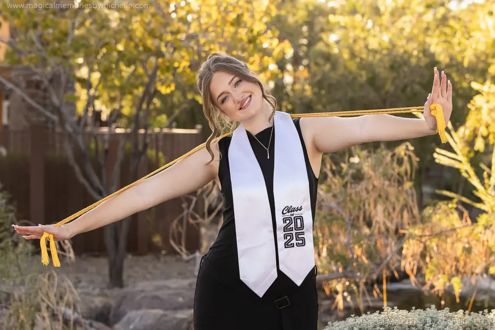 Senior girl wearing a black dress, white stole, and yellow cords during graduation pictures in Mesa, Arizona.