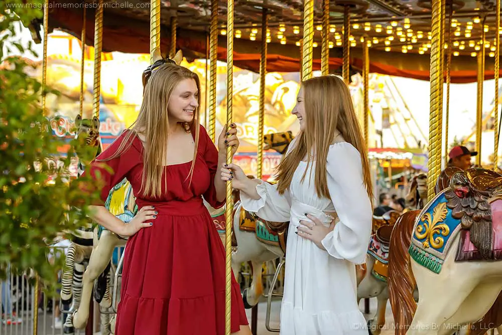 Two senior girls sharing a photo session at a carnival carousel to help reduce senior portrait costs.
