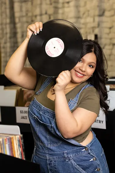 Latina senior girl smiling and holding a vinyl record during her photo session at a Mesa record store.