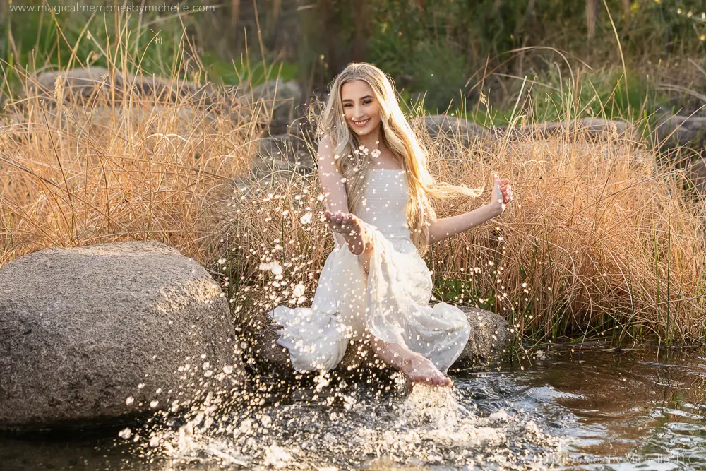 Senior girl in a white dress splashing water during a creative outdoor senior photo session in Arizona.
