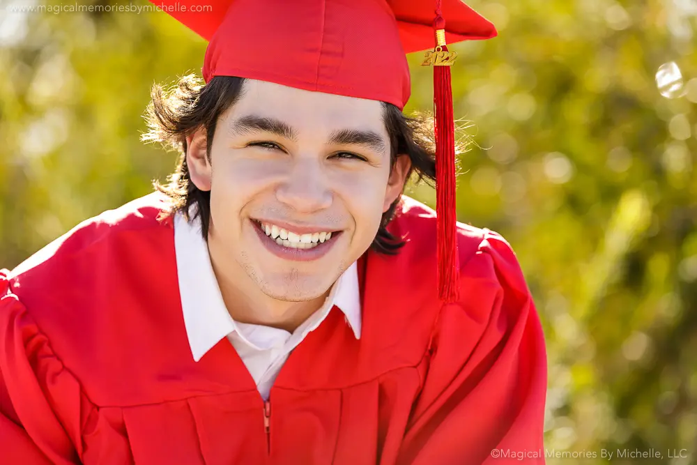 Smiling senior guy wearing a red cap and gown during graduation portraits in Mesa, Arizona.