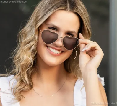 Senior girl smiling while wearing heart-shaped sunglasses during her photo session.