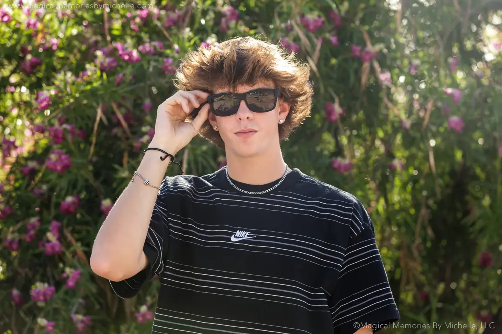 Senior boy wearing striped Nike shirt and sunglasses in front of flowering trees.