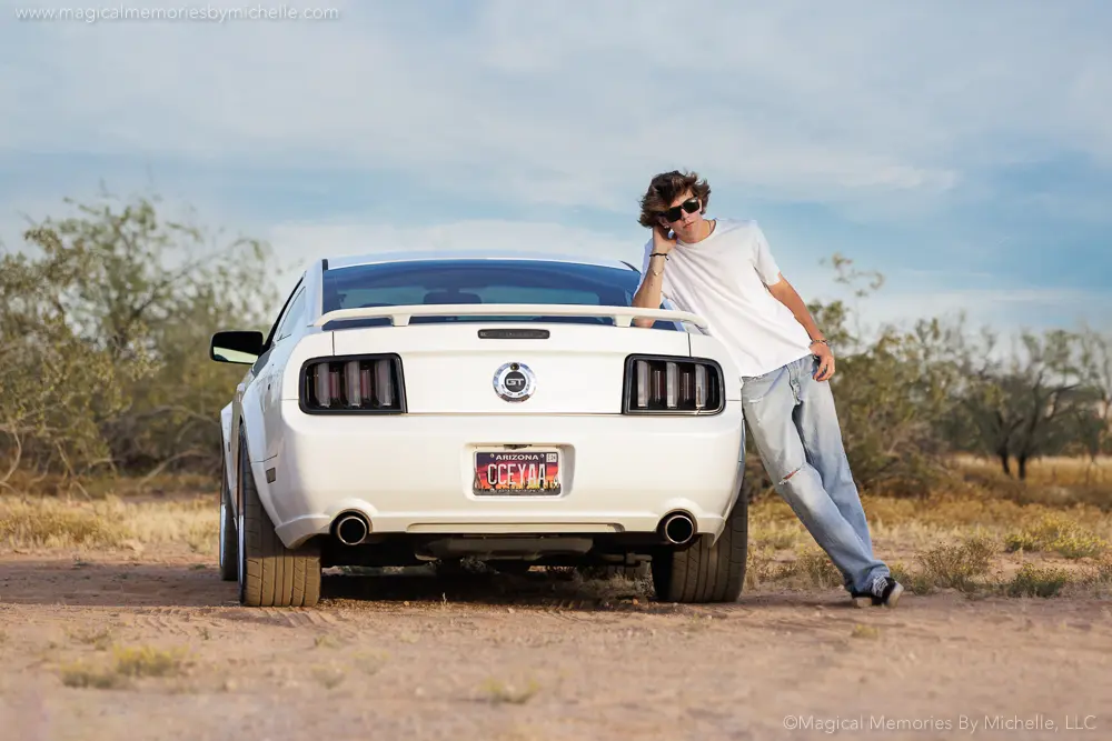 Senior guy leans against his white Mustang during a car-themed senior photo session in the Arizona desert.