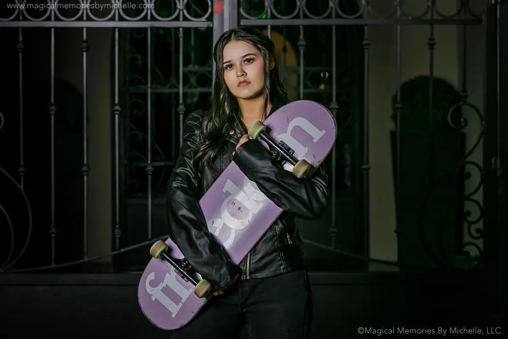 Chandler senior photographer captures an urban night portrait of a teen holding a skateboard and wearing a black leather jacket downtown.