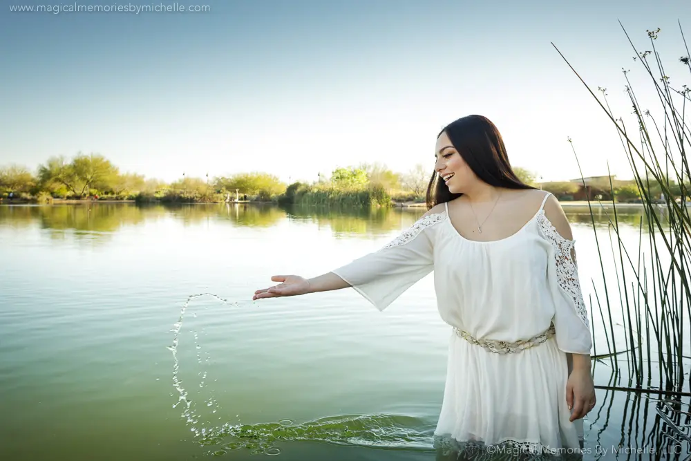 Chandler senior photographer captures a teen in a white boho dress playing with water at Veterans Oasis lake during golden hour.