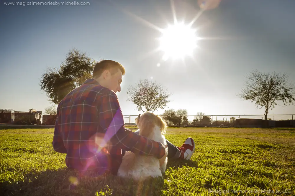 Chandler senior photographer captures a teen sitting on the grass with his dog at sunset, highlighting a playful pet‑friendly session.