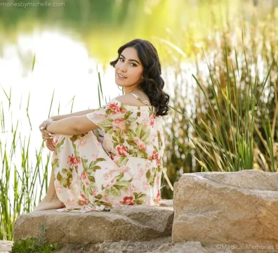 Senior girl in floral dress sitting on rocks by the lake at Veterans Oasis Park Chandler.
