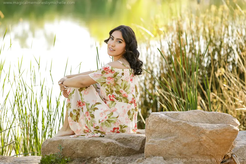 Senior girl in floral dress sitting on rocks by the lake at Veterans Oasis Park Chandler.