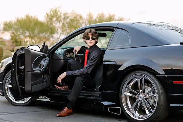 Senior guy in a black button-down shirt and red tie poses confidently in the driver’s seat of a black Mustang in Mesa, Arizona.