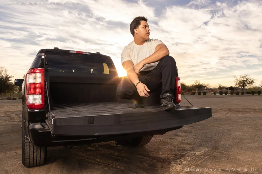 Senior boy sits on the tailgate of a black truck during sunset in Arizona, captured during his senior photo session.