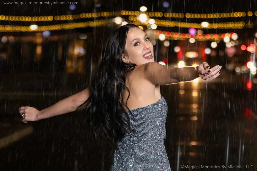 Senior girl twirling in the rain at night during a creative photo session with sparkling city lights.