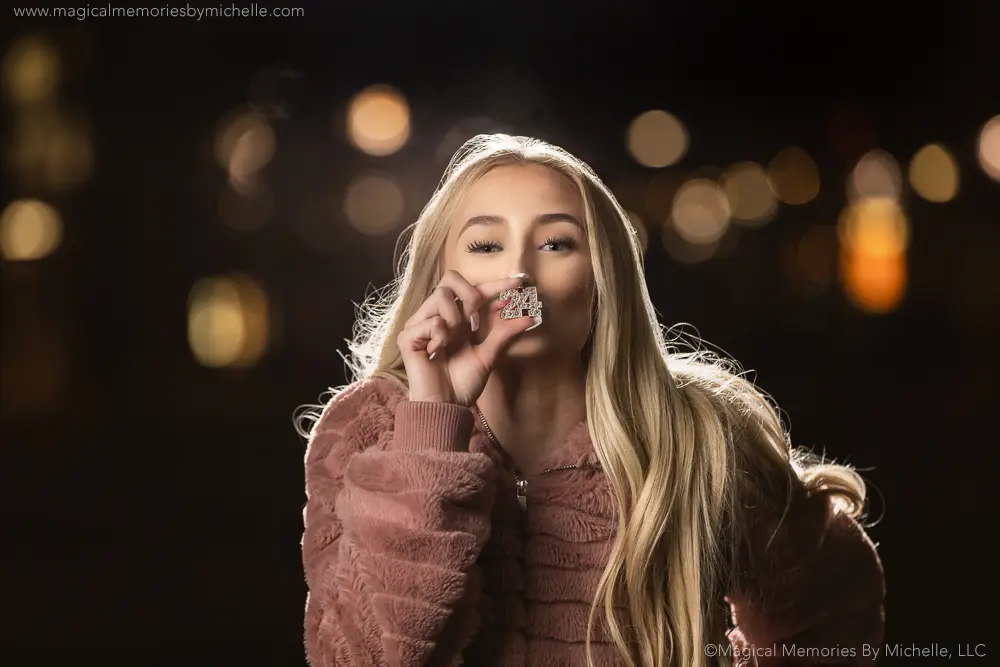 Senior girl in focus with blurry city lights in the background, captured at 200mm and f/4 for a compressed portrait look.