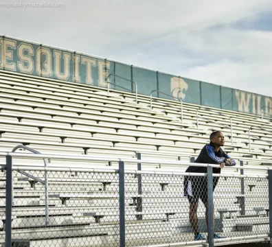 Senior boy leaning on a railing in front of bleachers that say Mesquite Wildcats.