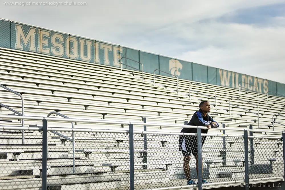 Senior boy leaning on a railing in front of bleachers that say Mesquite Wildcats.
