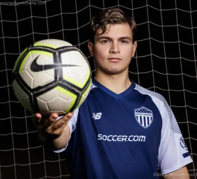Senior soccer player holding a ball in front of the net during a nighttime portrait session wearing his AYSO United jersey.