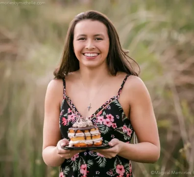 Teen girl in a floral dress smiles while holding a mini birthday cake during her outdoor Sweet 16 photo shoot in Mesa, Arizona.