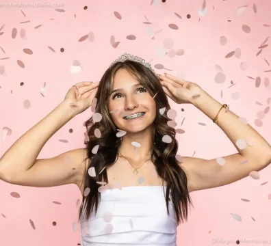 Teen girl wearing a tiara and white dress smiles as confetti falls during her Sweet 16 photo shoot in Mesa, AZ.