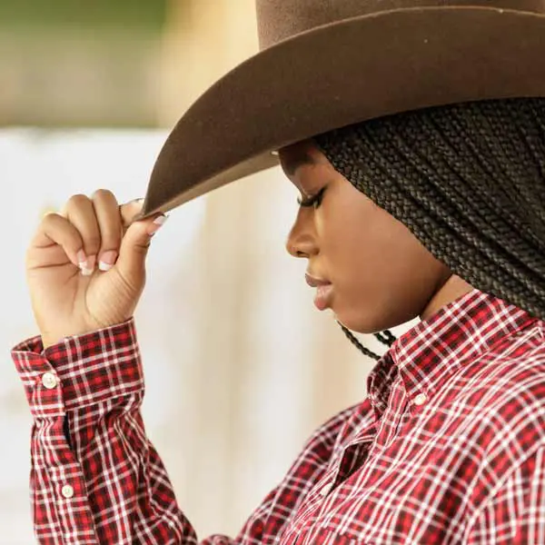 Senior girl in plaid shirt and cowboy hat posing for country-style portraits.
