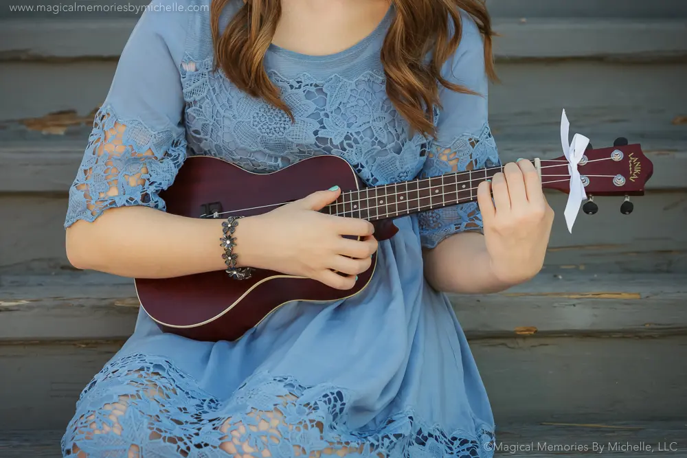 Close‑up of a senior girl holding a ukulele while wearing a blue lace dress during her Downtown Mesa senior photos.