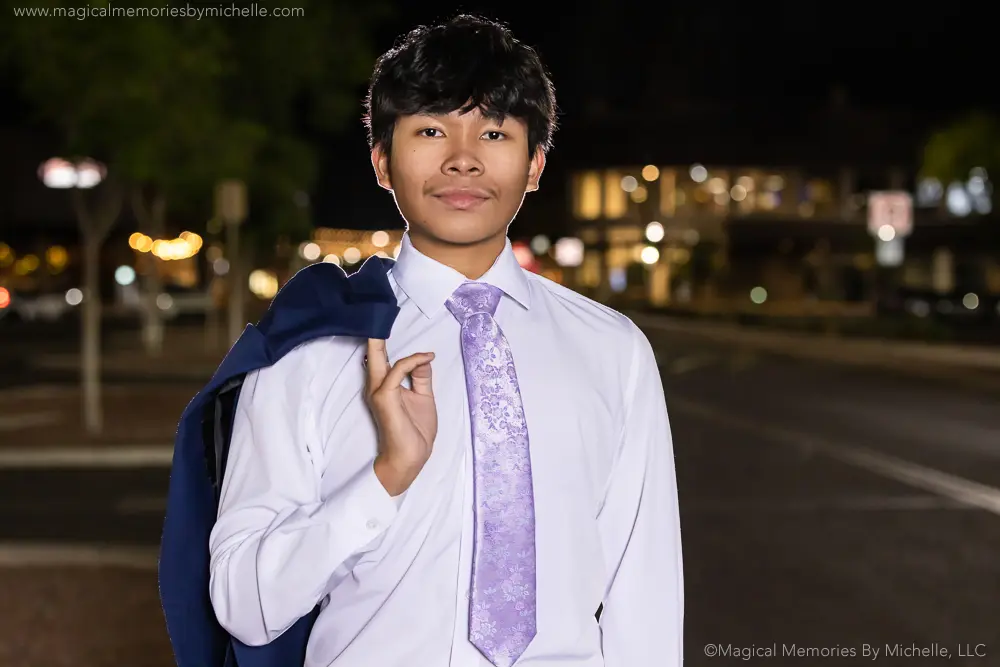 Senior guy wearing a white dress shirt and lavender tie with jacket over shoulder during nighttime senior pictures in Mesa, Arizona.