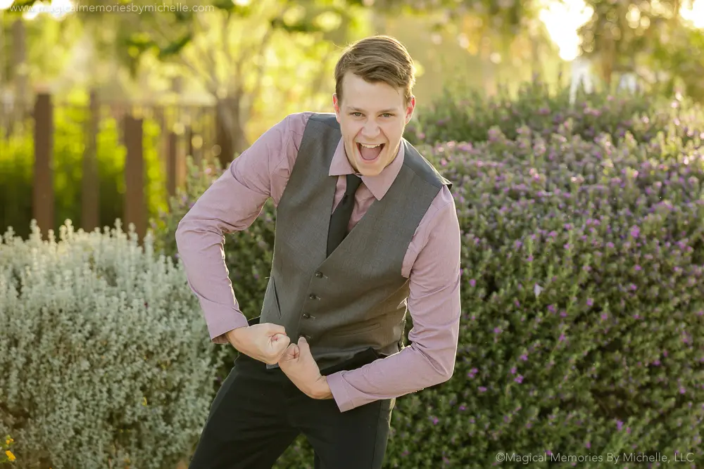 Senior boy wearing a gray vest and tie flexing and smiling during playful formal senior pictures in Mesa, Arizona.