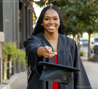 Smiling Black high school senior in cap and gown tosses her graduation cap toward the camera during her senior photo session in Downtown Gilbert, Arizona.
