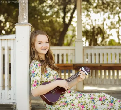 Senior girl sitting with her ukulele against a gazebo post in Downtown Mesa.